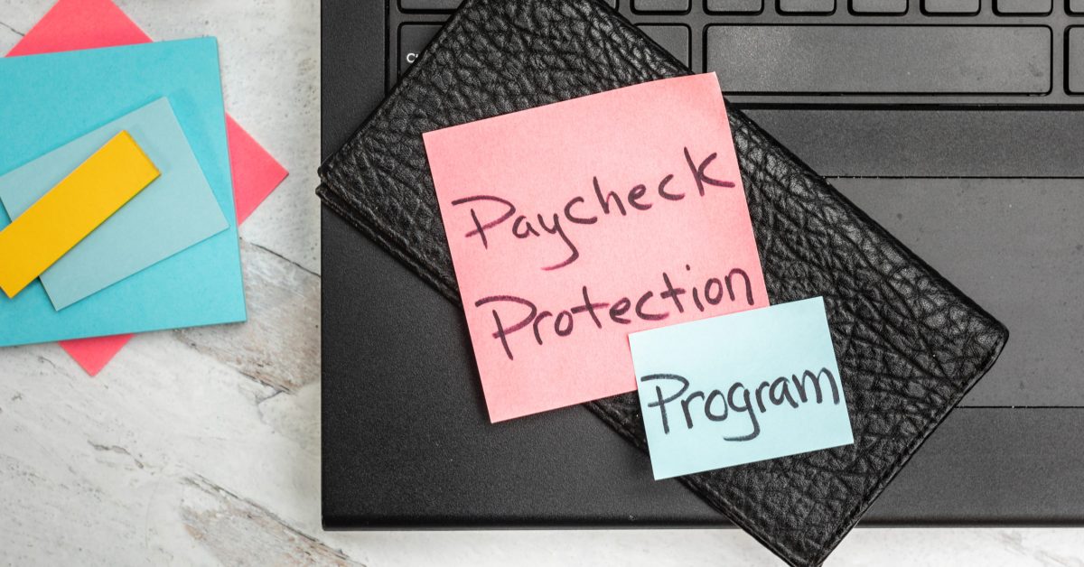 Paycheck protection program posted notes lab top and office supplies in the background