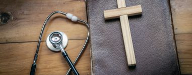 Close up the cross on Bible with stethoscope on wooden table, christian treatment concept.